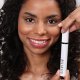 Eine Frau präsentiert selbstbewusst eine Tube Mascara und präsentiert ihr Schönheitsprodukt mit einem strahlenden Lächeln.