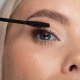 Eine Frau trägt mit einer Mascara-Bürste vorsichtig Mascara auf ihre Wimpern auf und verbessert so ihr Augen-Make-up präzise.