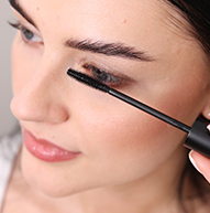Eine Frau trägt die Wimperntusche gekonnt mit einer Mascara-Bürste auf und konzentriert sich dabei auf ihre Wimpern, um einen definierten Look zu erzielen.